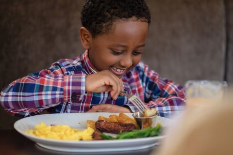 A Boy Sitting At A Table With A Plate Of Food